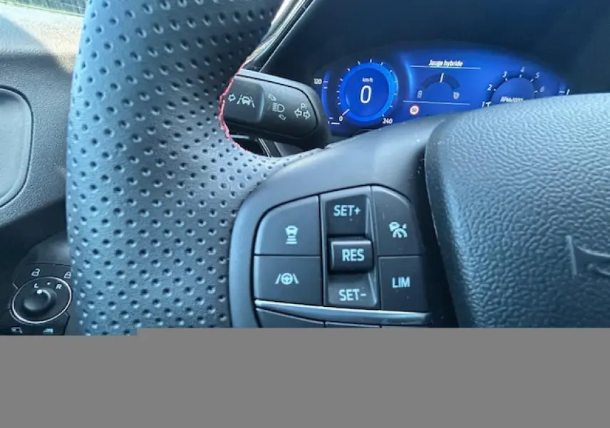 Gros plan sur le volant perforé noir avec surpiqûres rouges et le combiné d'instrumentation numérique bleu du Ford Puma 2023.