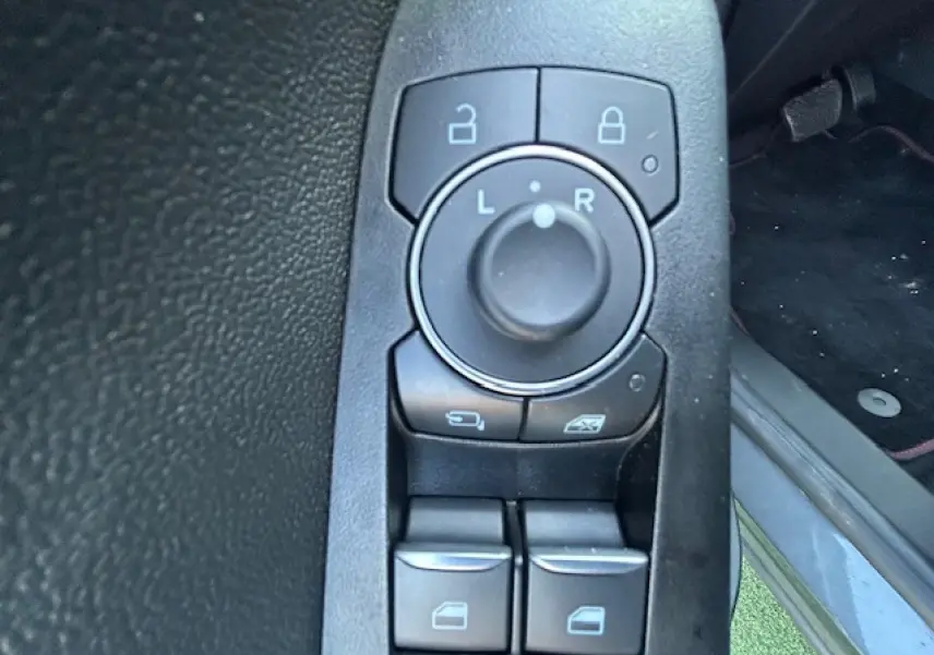 Gros plan sur les commandes de réglage des rétroviseurs et des vitres côté conducteur du Ford Puma noir Agate 2023.