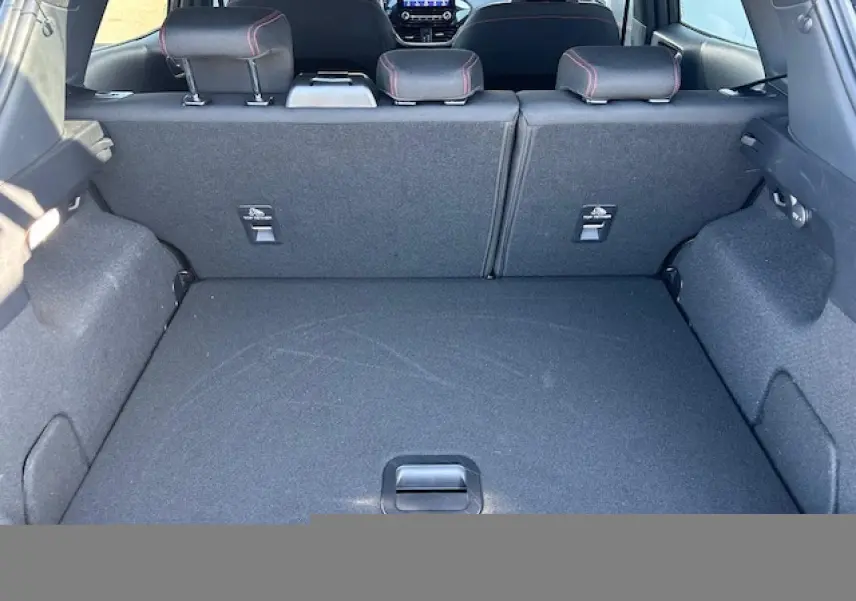 Vue intérieure du coffre du Ford Puma noir Agate, montrant la banquette arrière rabattable avec surpiqûres rouges visibles sur les appuie-têtes.