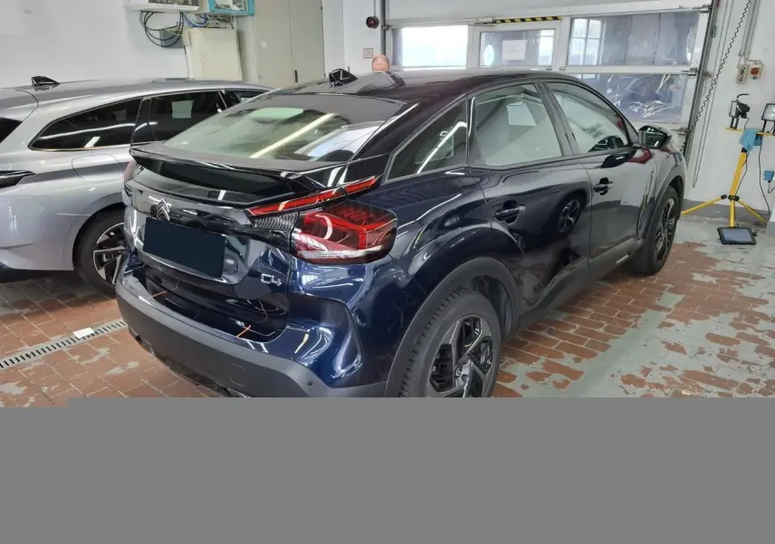 Vue 3/4 arrière droite d'une Citroën C4 2024 bleu Eclipse avec toit noir Perla dans un garage.