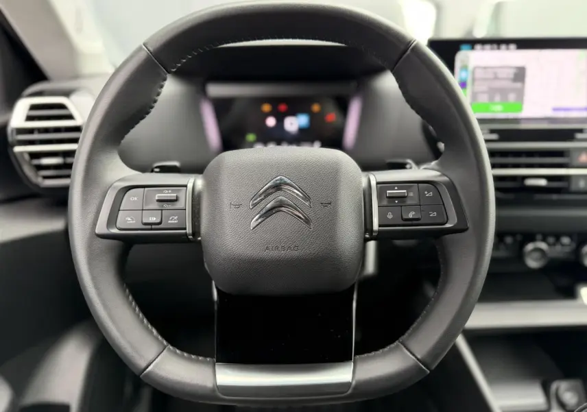 Vue frontale du volant cuir noir de la Citroën C4 2024 avec commandes intégrées et tableau de bord numérique flou.