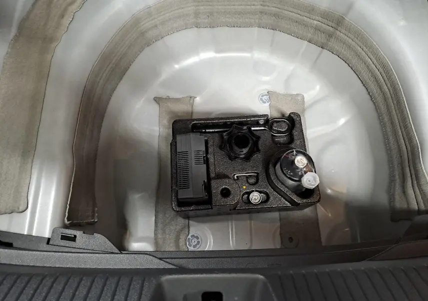 Vue plongeante sur le coffre ouvert d'un Volkswagen Taigo blanc, montrant le kit de dépannage rangé dans la roue de secours.