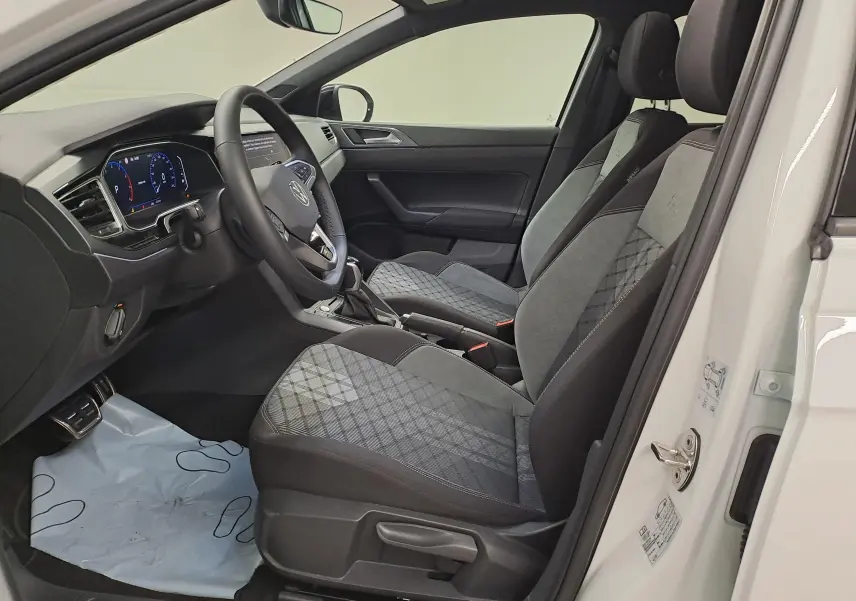 Vue intérieure côté conducteur du Volkswagen Taigo blanc pur, sièges sport gris à motifs et tableau de bord digital.