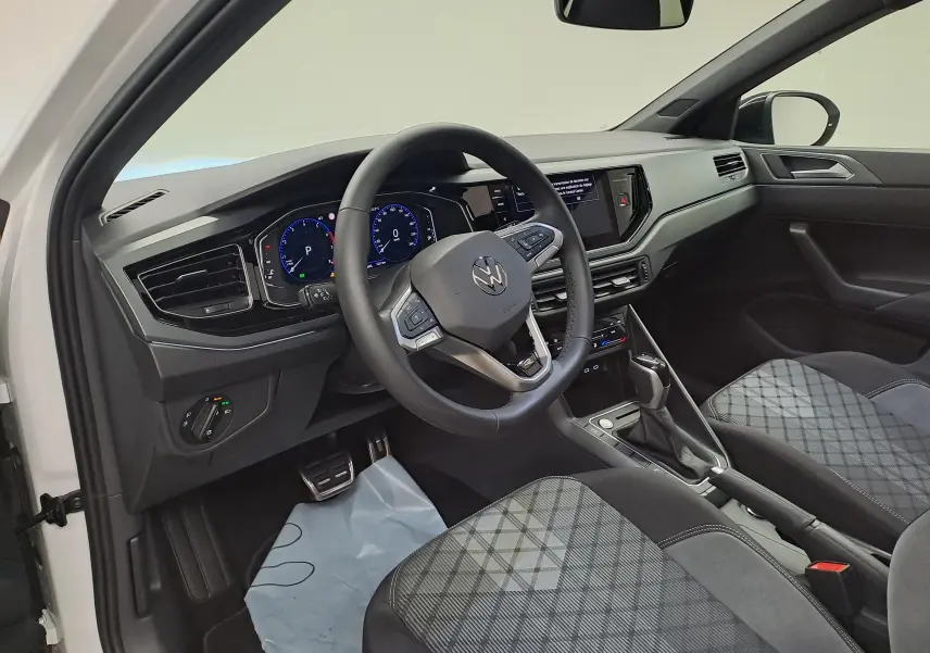 Vue intérieure côté conducteur du Volkswagen Taigo 2025, volant cuir multifonctions et sièges tissu à motif gris.