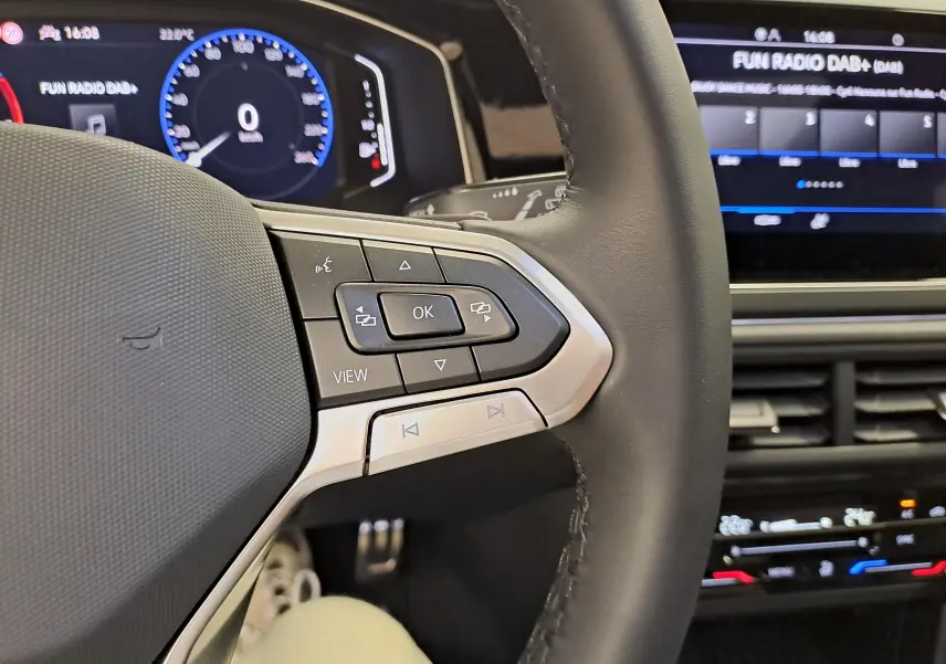 Gros plan sur le volant cuir multifonctions du Volkswagen Taigo 2025, avec tableau de bord digital et écran tactile en arrière-plan.