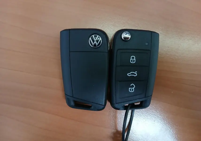 Clé de voiture Volkswagen noire vue de face et de dos posée sur une surface en bois clair.