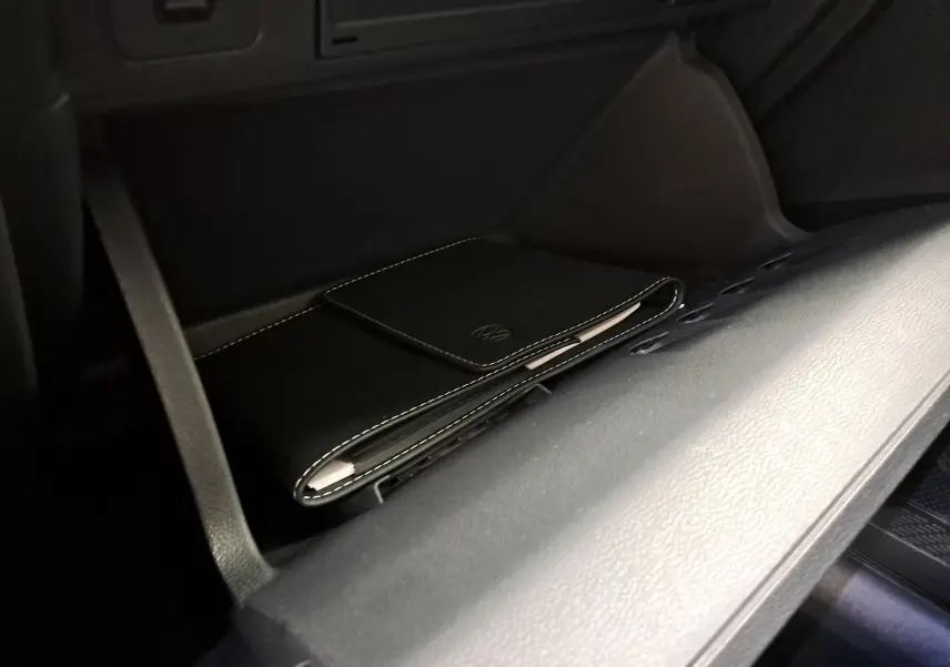 Détail de la boîte à gants ouverte avec pochette noire siglée Volkswagen dans un Volkswagen Taigo blanc toit noir.