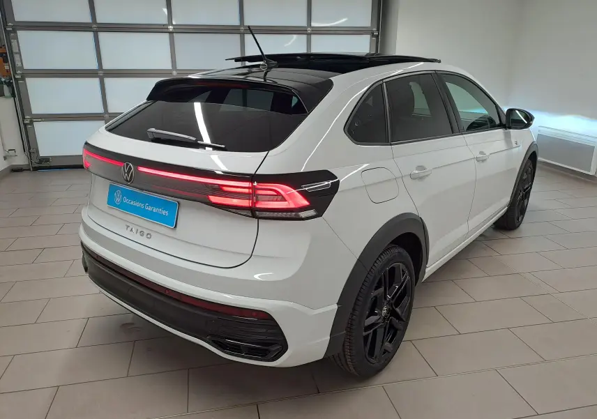Vue 3/4 arrière droite du Volkswagen Taigo blanc pur avec toit noir, jantes noires et feux arrière allumés en intérieur.
