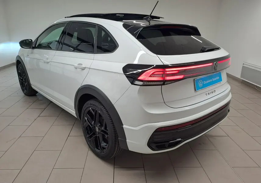 Vue 3/4 arrière droite du Volkswagen Taigo blanc pur avec toit noir et jantes noires R-Line dans un showroom.