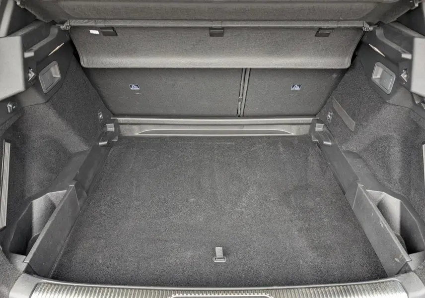 Coffre ouvert vu de face, intérieur noir avec tapis et rangements latéraux, sans chargement visible.