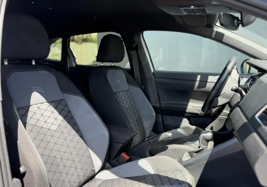 Vue intérieure côté gauche du Volkswagen Taigo TSI 116 DSG R-Line 2025, sièges sport tissu gris avec surpiqûres et logo R-Line.