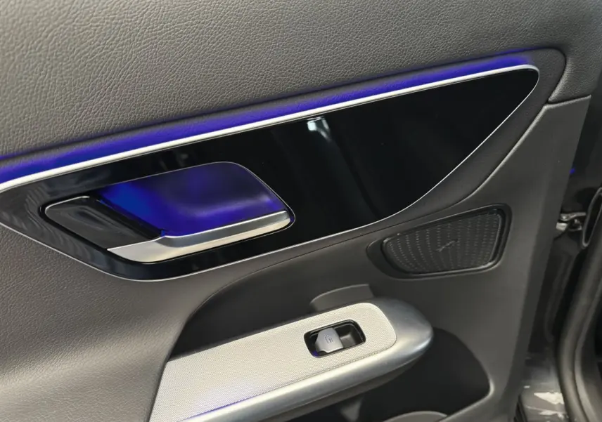 Gros plan sur la poignée intérieure et le panneau de porte côté conducteur du Mercedes GLC gris foncé avec éclairage d'ambiance bleu.
