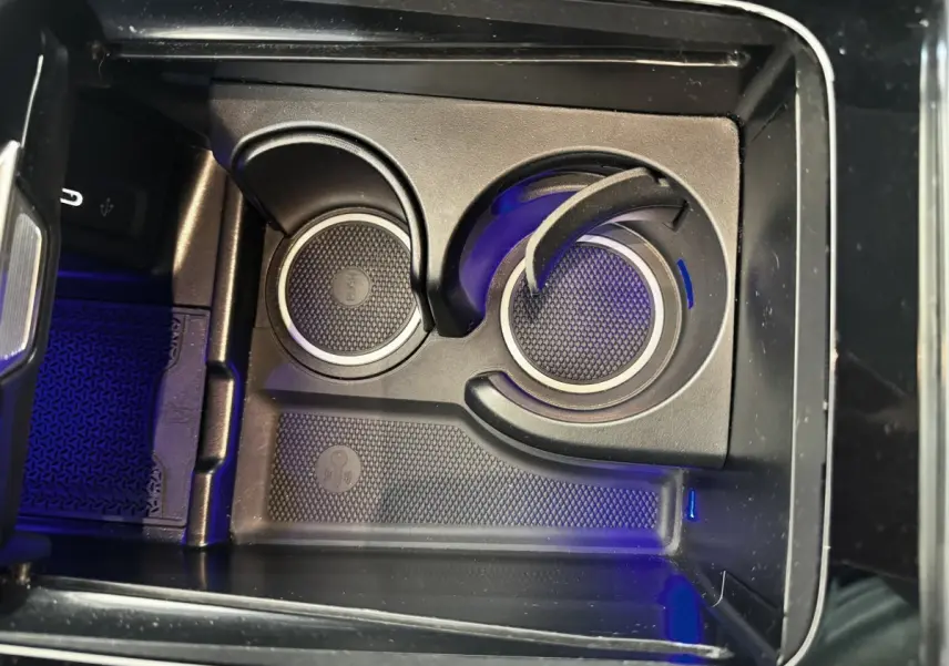 Gros plan sur les porte-gobelets noirs avec éclairage bleu à l'intérieur de la console centrale du Mercedes GLC 300 E gris foncé.