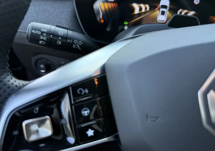 Gros plan sur le volant et la commande des phares du MG MOTOR ZS Hybrid gris foncé, avec affichage numérique en arrière-plan.