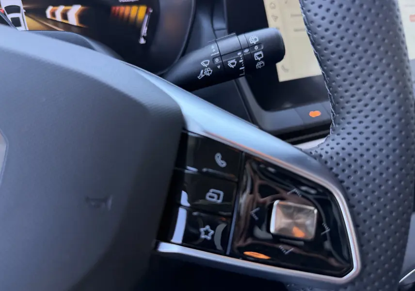 Gros plan sur le volant perforé gris foncé du MG MOTOR ZS Hybrid 2026, avec commandes multifonctions et tableau de bord numérique en arrière-plan.