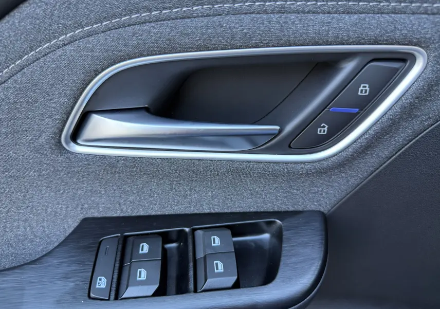 Gros plan sur la poignée intérieure et les commandes de fenêtre côté conducteur du MG Motor ZS Hybrid 197 gris foncé.