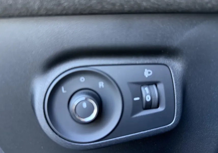 Gros plan sur les commandes de réglage des rétroviseurs électriques dans un MG Motor ZS Hybrid gris foncé, intérieur côté conducteur.