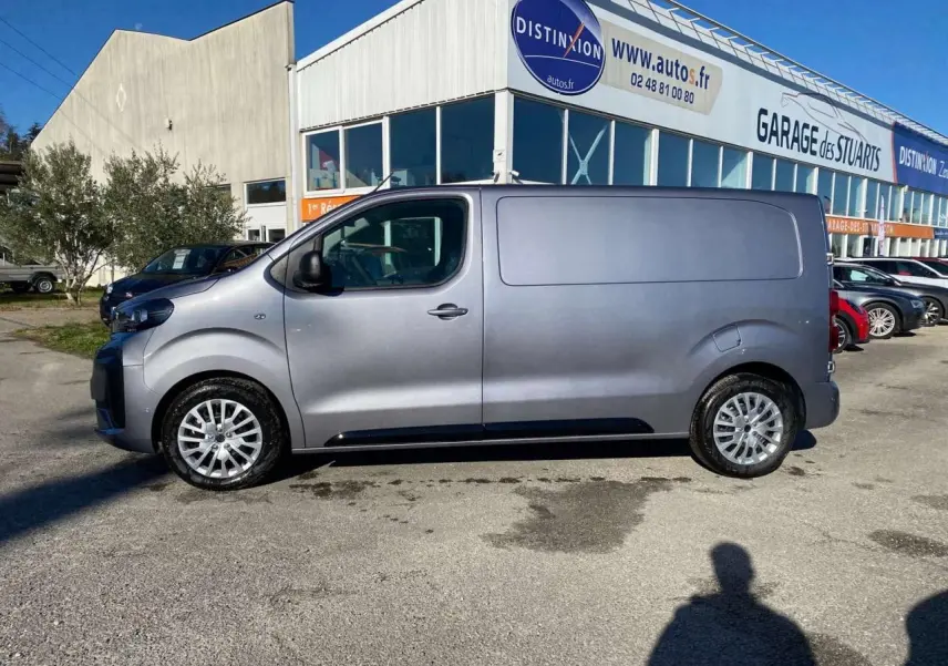 Peugeot Expert Fourgon gris Artense vu de profil côté gauche, stationné devant un garage en extérieur.