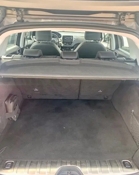 Vue depuis le coffre ouvert d'un Peugeot 2008 gris, montrant l'habitacle et la tablette cache-bagages déployée.
