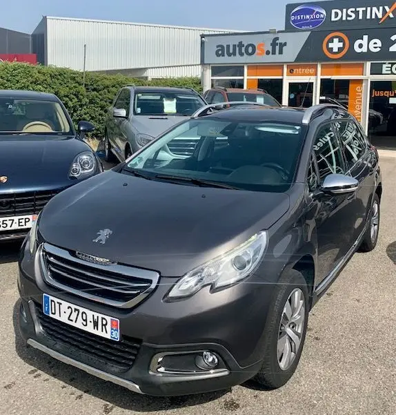 Peugeot 2008 gris foncé vue 3/4 avant droit, avec calandre chromée et toit noir, stationnée devant un concessionnaire autos.fr