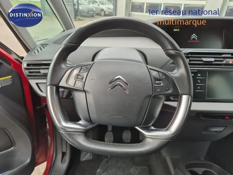 Vue rapprochée du volant cuir multifonction noir du Citroën Grand C4 Spacetourer rouge Rubi, avec tableau de bord moderne.