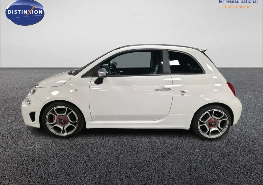 Profil droit de l'Abarth 500 blanc avec étriers rouges et jantes alliage 17 pouces dans un showroom intérieur.