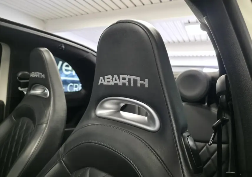 Gros plan sur les sièges avant en cuir noir avec logo ABARTH brodé, intérieur de l'Abarth 595C Turismo blanc.