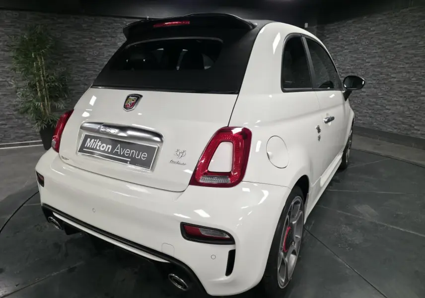 Vue 3/4 arrière droite de l'Abarth 595C Turismo blanche avec toit noir et étriers de frein rouges visibles.