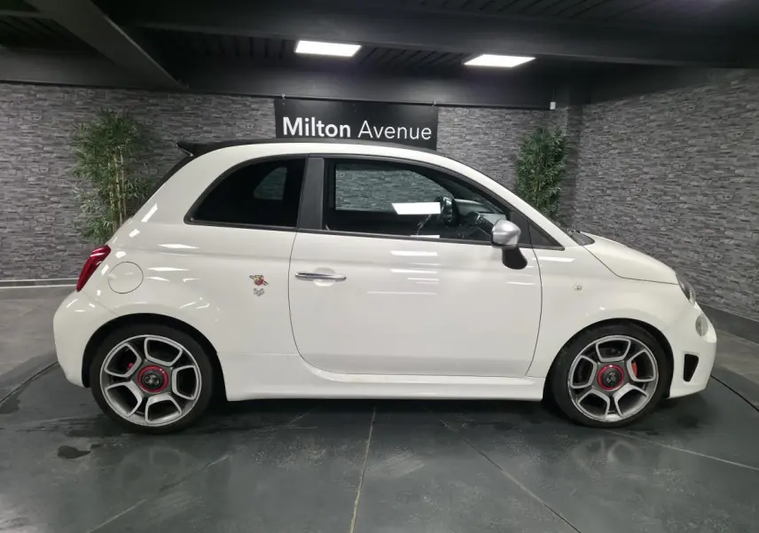 Profil droit d'une ABARTH 500 blanche avec jantes 17 pouces et étriers de frein rouges, dans un showroom intérieur.