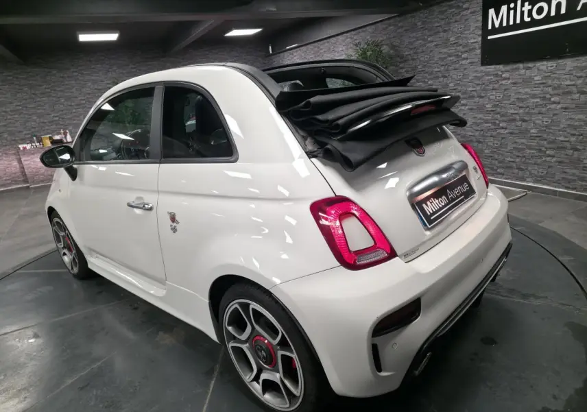Vue 3/4 arrière droite d'une ABARTH 595C Turismo blanche avec toit ouvrant replié et étriers de frein rouges.