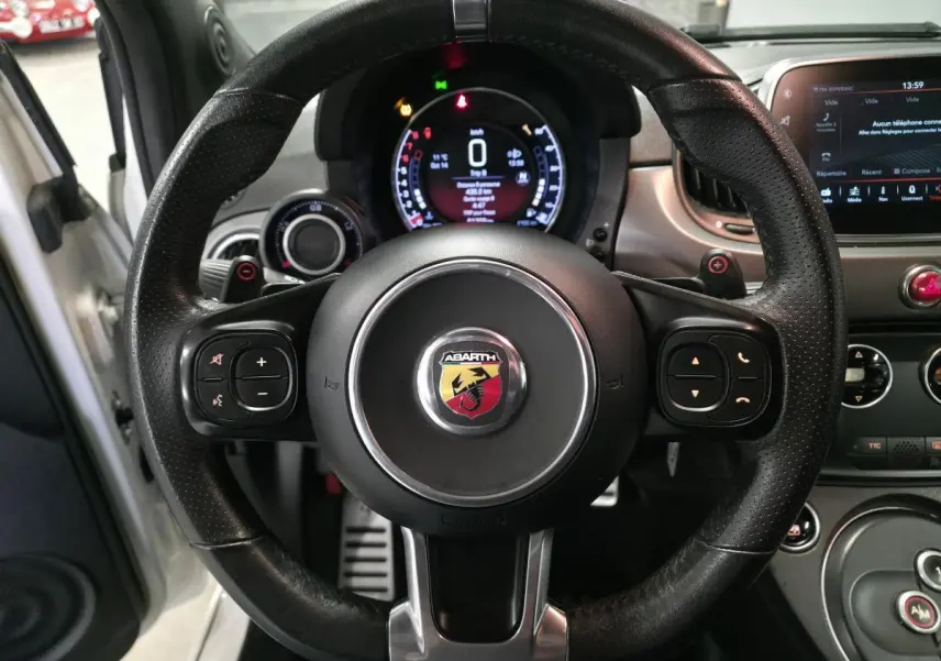 Vue centrée sur le volant cuir perforé noir de l'Abarth 595C blanc, avec tableau de bord numérique et écran tactile visible.