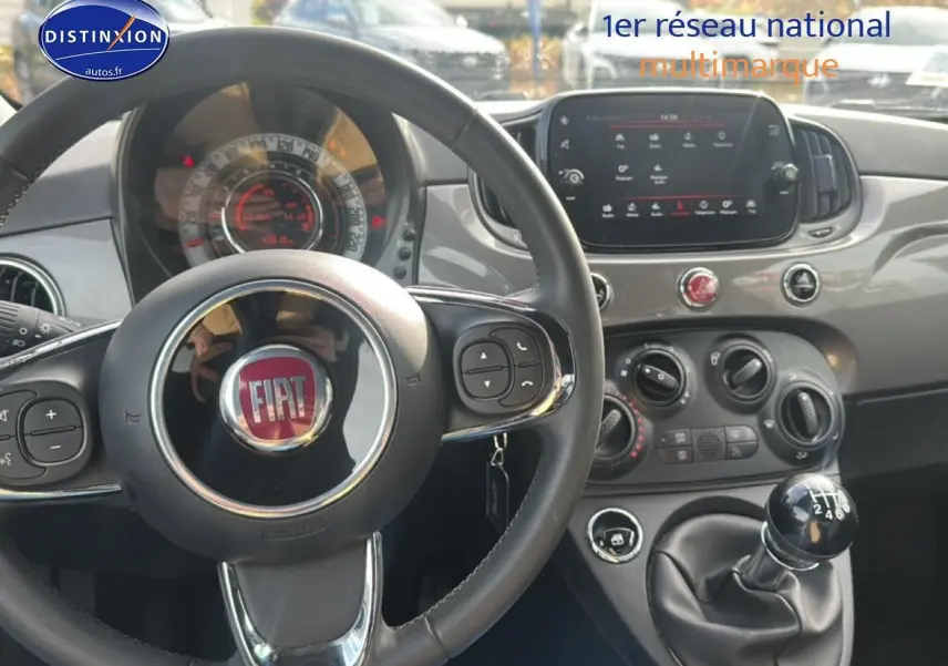 Vue intérieure centrée sur le volant noir et la console centrale grise avec écran tactile et levier de vitesses manuel.