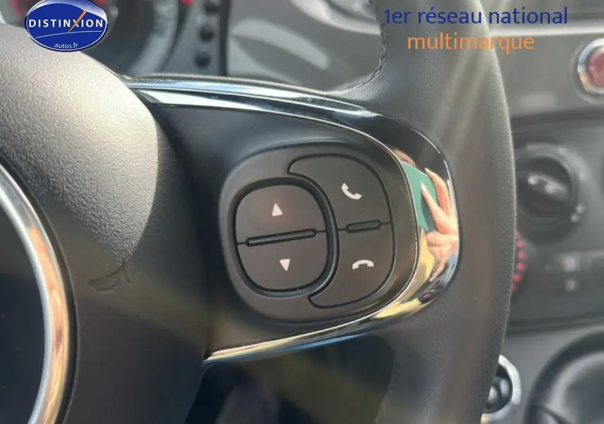 Gros plan sur les commandes audio au volant cuir de la FIAT 500 gris, avec tableau de bord flou en arrière-plan.