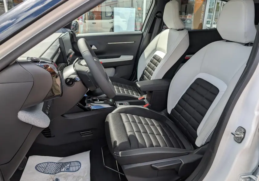 Vue intérieure côté conducteur du Citroën C3 Aircross blanc, sièges bicolores noir et gris avec console centrale et volant multifonctions.