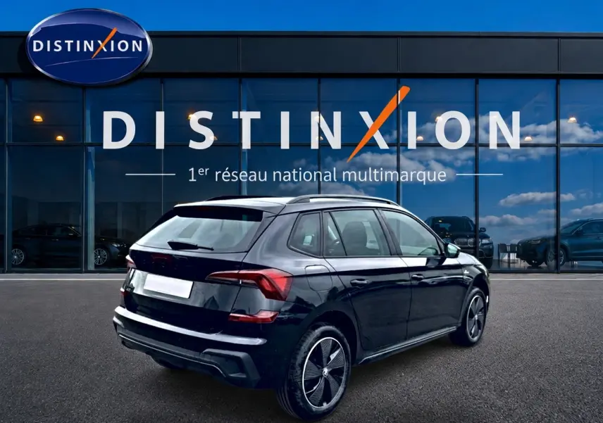 Vue 3/4 arrière droite d'un Skoda Kamiq noir 2026 avec jantes alu et barres de toit devant une vitrine Distinxion.