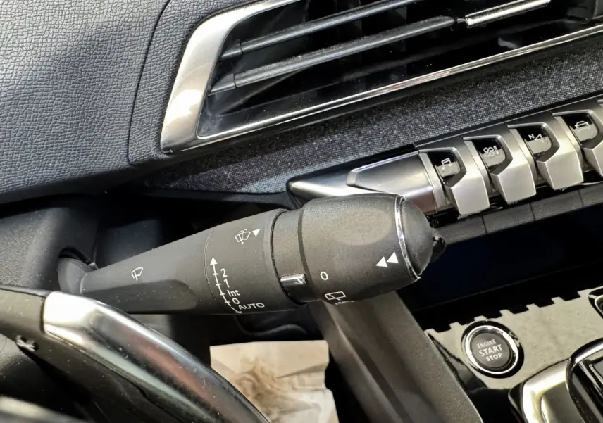 Gros plan sur la commande d’essuie-glace noire et les boutons de la console centrale d’un Peugeot 5008 noir, intérieur avant.