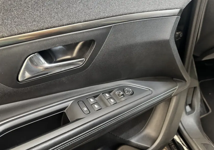 Gros plan sur la porte intérieure côté conducteur du Peugeot 5008 noir, avec commandes des vitres et poignée chromée.