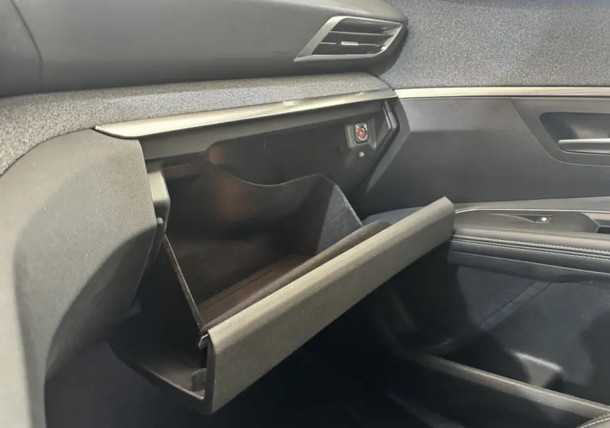 Gros plan sur la boîte à gants ouverte côté passager du Peugeot 5008 noir, soulignant les finitions intérieures modernes.