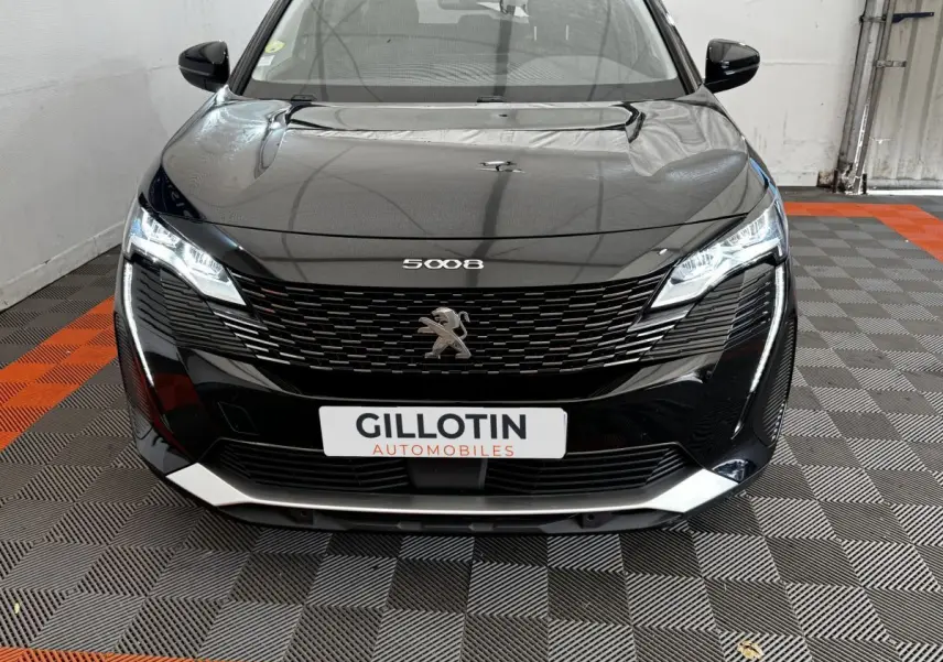 Vue frontale d'un Peugeot 5008 noir 2022 avec calandre distinctive et phares LED allumés dans un garage.
