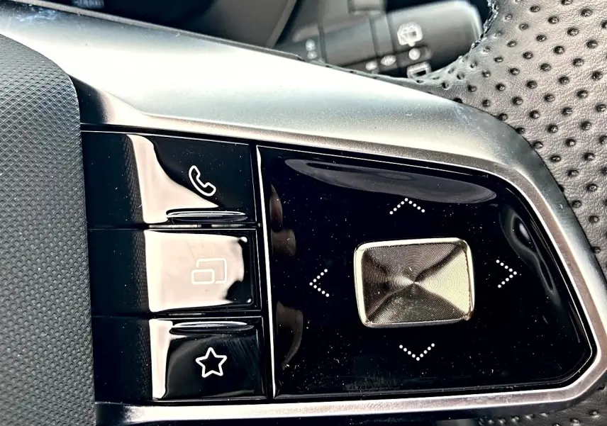 Gros plan sur les commandes noires et argentées au volant perforé du MG Motor ZS 1.5 hybrid 197 luxury.