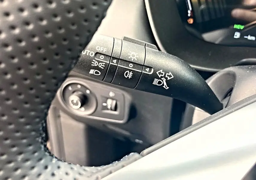 Gros plan sur la commande de phares et clignotants à gauche du volant perforé dans l’habitacle noir du MG ZS 1.5 hybrid 197 luxury.