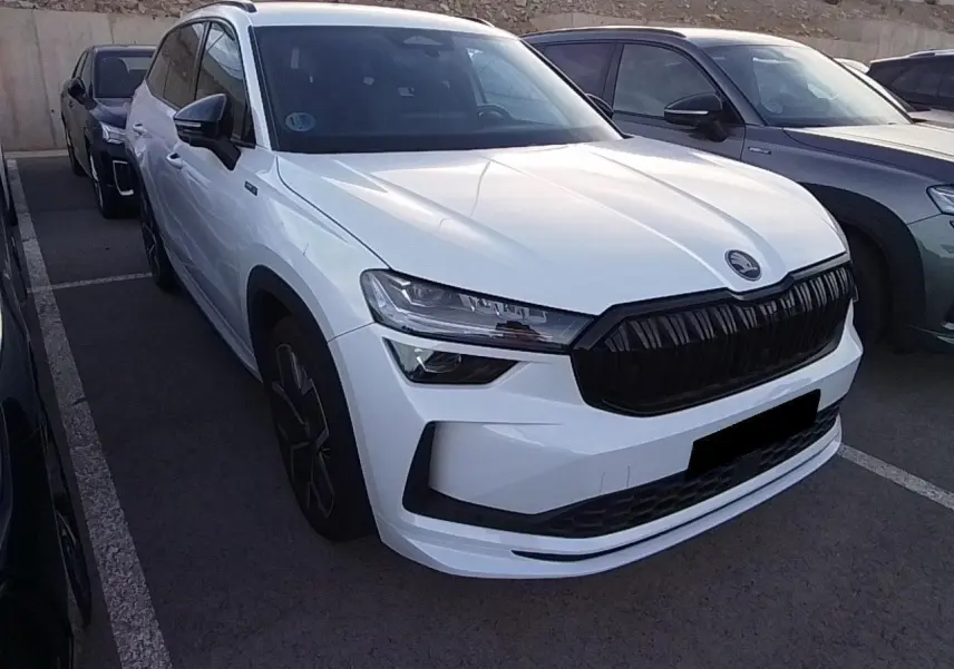 Vue 3/4 avant d'un Skoda Kodiaq blanc Glacier avec calandre noire et jantes alliage anthracite, stationné en extérieur.
