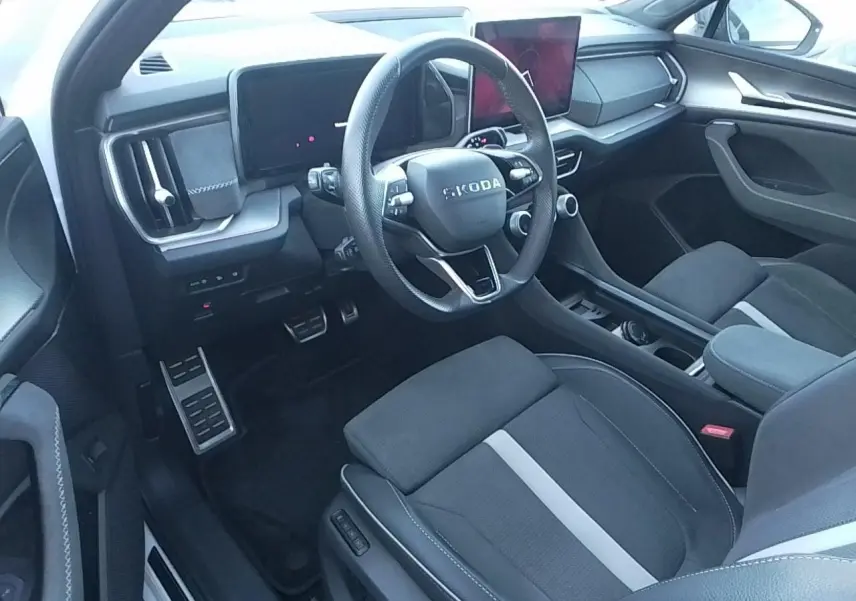 Vue intérieure côté conducteur du Skoda Kodiaq 2025, volant sport, sièges tissu suédine noir avec bande blanche, tableau de bord moderne.