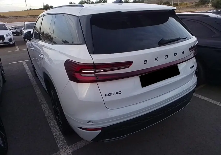Vue 3/4 arrière gauche d’un Skoda Kodiaq blanc Glacier avec feux arrière LED et vitrage surteinté.