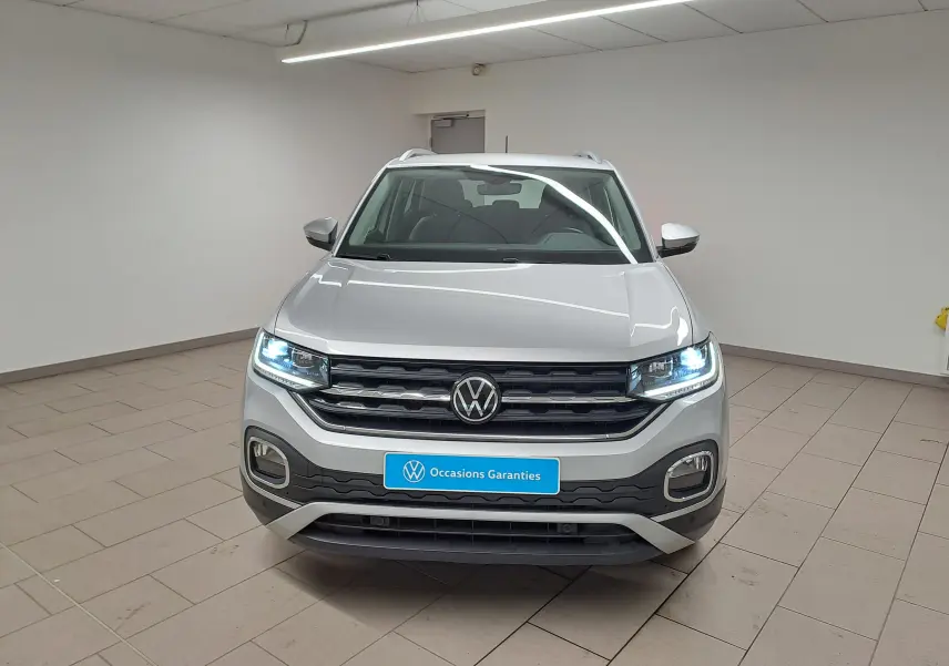 Vue avant d'un Volkswagen T-Cross 1.0 TSI 110 DSG7 Style en peinture métallisée Reflet d'argent avec phares allumés en intérieur.