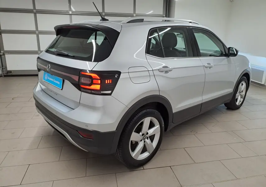 Vue 3/4 arrière droite du Volkswagen T-Cross 2022 en peinture métallisée Reflet d'argent avec feux arrière allumés.