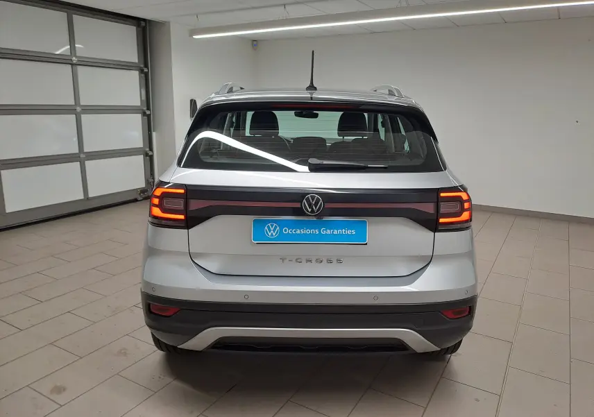 Vue arrière d'un Volkswagen T-Cross 2022 argent métallisé avec feux allumés, dans un garage intérieur.