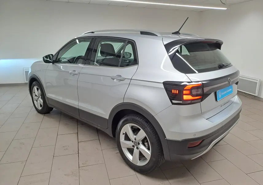 Vue 3/4 arrière droite d’un Volkswagen T-Cross 2022 couleur reflet d’argent avec feux arrière allumés en intérieur.