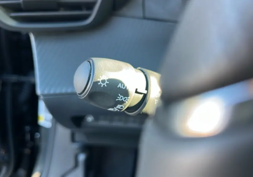 Gros plan sur la commande des feux au volant d’un Peugeot 2008 noir perla nera, intérieur moderne et lumineux.