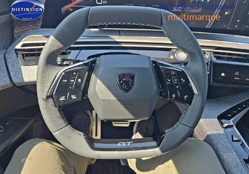 Vue intérieure centrée sur le volant cuir perforé gris du Peugeot 5008 Hybrid 145 GT avec tableau de bord numérique.